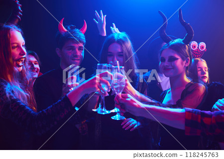 Halloween party scene at dimly lit nightclub with young people dressed in various costumes, with spooky makeup, enjoying night of fun, games, and drinks 118245763