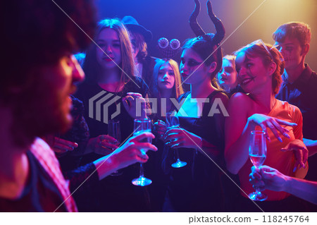 Group of young friends, dressed in spooky and fun costumes, attending nightclub for cheerful celebration of Halloween 118245764