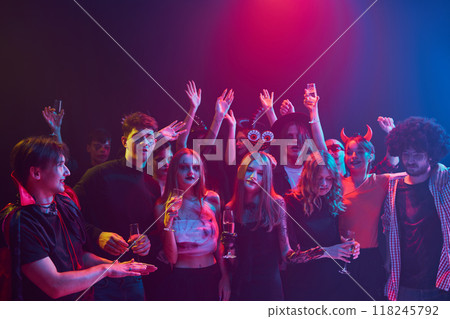 Lively group of young people, men and women attending night club for Halloween party, showing off their costumes and enjoying night filled with music and dancing 118245792