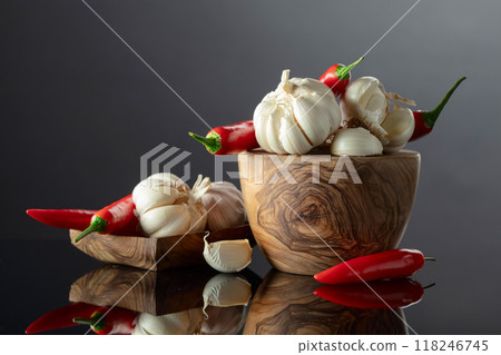 Garlic bulbs and red chili peppers in wooden dishes on a black background. Garlic bulbs and red chili peppers in wooden dishes on a black background. 118246745
