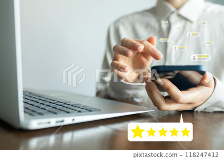 A man is using a cell phone while sitting at a desk with a laptop A man is using a cell phone while sitting at a desk with a laptop 118247412