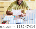 A man is sitting at a desk with a laptop and a stack of papers 118247414