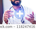 A man wearing a white lab coat is holding a stethoscope and smiling 118247416