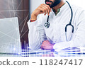 A doctor is sitting at a desk with a laptop and a stethoscope 118247417