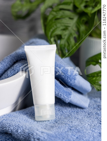 White cream tube on blue folded towel near vessel basin close up in bathroom, cosmetic mockup 118247770