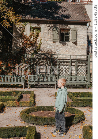 Little boy is Standing in front of House with nice garden in autumn season. Flowers in the City Park of Bietigheim-Bissingen, Baden-Wuerttemberg, Germany, Europe. Autumn Park and house, nobody, bush 118248338