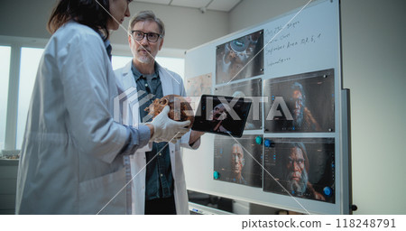 Male and female scientists study anatomy of fossil skull of ancient man using tablet computer Male and female scientists study anatomy of fossil skull of ancient man using tablet computer 118248791