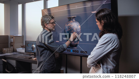 Archaeologists discuss study cultural artifact. Big screen shows 3D visualization ancient clay vase 118248807