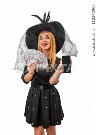 Excited young witch holding a fan of money and showing a smartphone with a blank screen is isolated on a white background 118248906