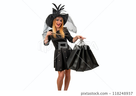 Young witch conjures shopping bags with her wand, looking happy in a black costume against a white background. Celebrate Halloween with magic and retail therapy 118248937