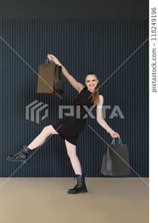 Happy cheerful young woman with black shopping bags takes a long step, seasonal discount. Full length portrait, vertical frame. Black friday, sales 118249196