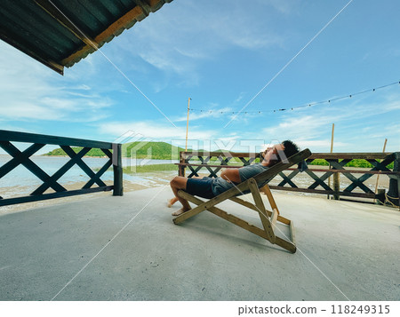 Man leaning on the beach chair, resting on the homestay terrace by the sea. Man leaning on the beach chair, resting on the homestay terrace by the sea. 118249315