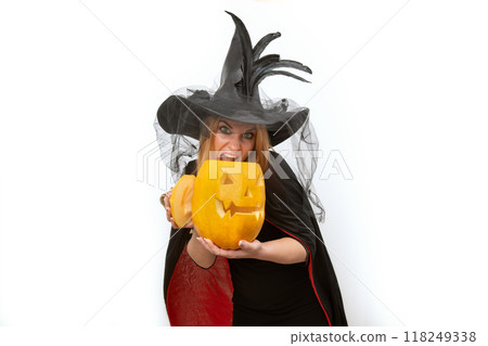 Crazy screaming young woman with jack-o'-lantern in hands and witch hat. Space for text, white background. Black clothes. Halloween Party. Crazy screaming young woman with jack-o'-lantern in hands and witch hat. Space for text, white background. Black clothes. Halloween Party. 118249338