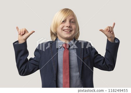Portrait of young Caucasian boy with blond hair, dressed in blue shirt and red tie, make shaka gesture and smiles broadly, has pleasant expression, isolated over white background. Emotions concept Portrait of young Caucasian boy with blond hair, dressed in blue shirt and red tie, make shaka gesture and smiles broadly, has pleasant expression, isolated over white background. Emotions concept 118249455