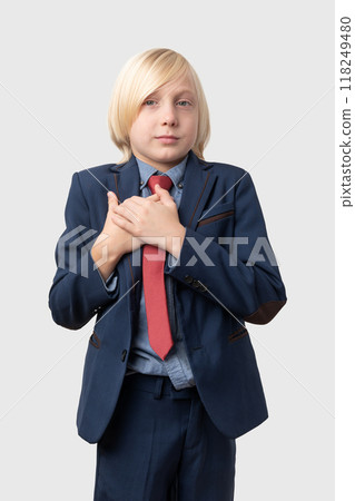 Portrait of young businesswoman with blond hair, dressed in blue suit and red tie, keeps hands on chest isolated on white background Portrait of young businesswoman with blond hair, dressed in blue suit and red tie, keeps hands on chest isolated on white background 118249480