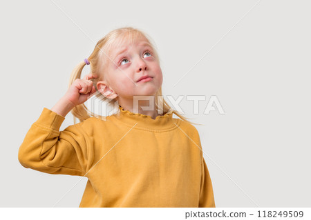 Portrait of cute little girl with ponytail in yellow sweater looking up and thinking about something while standing against grey background Portrait of cute little girl with ponytail in yellow sweater looking up and thinking about something while standing against grey background 118249509