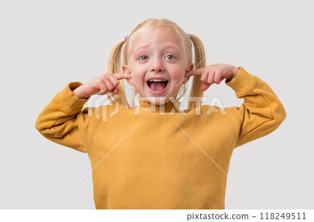 Portrait of a little girl with two ponytails wearing a yellow sweater and making funny faces 118249511
