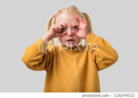 Portrait of a cute little girl looking through her fingers like binoculars on a gray background Portrait of a cute little girl looking through her fingers like binoculars on a gray background 118249522