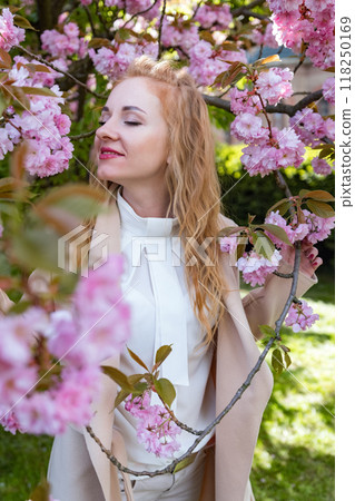 Happy young woman with closed eyes in park among flowering trees . Attractive red-haired girl in blooming park. Vertical frame. Happy young woman with closed eyes in park among flowering trees . Attractive red-haired girl in blooming park. Vertical frame. 118250169