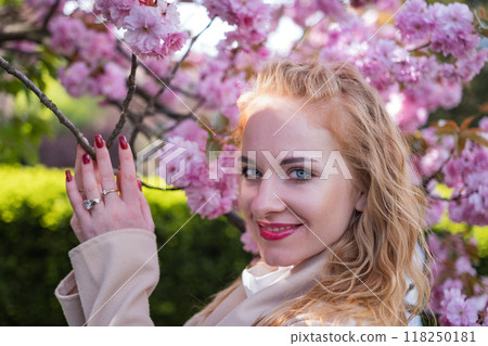 Portrait of happy young woman on flowering tree background. Portrait of charming fashionable girl in blooming sakura park. 118250181