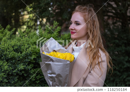 Beautiful young woman holding bouquet of yellow tulips. Woman with flowers in park waiting for someone. Lonely girl 118250184