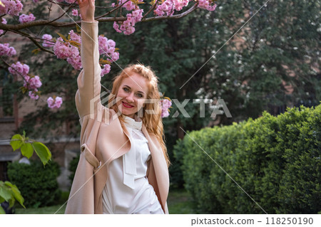 Attractive smiling young woman outdoor. Cheerful young girl walks in the spring blooming park has fun and dances. 118250190