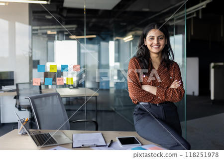 Portrait of young beautiful Latin American business woman, company employee smiling and looking at camera with crossed arms, businesswoman satisfied with work inside office using laptop. Portrait of young beautiful Latin American business woman, company employee smiling and looking at camera with crossed arms, businesswoman satisfied with work inside office using laptop. 118251978