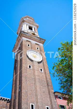 The Campanile dei Santi Apostoli rises 47 meters in the Cannaregio district of Venice, showcasing its historical architecture against a bright blue sky on a sunny day. 118252029