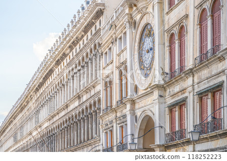 The early Renaissance St Marks Clocktower graces the Piazza San Marco's entrance with its intricate design and colorful clock. Tourists stroll by, enjoying the historic architecture of Venice. 118252223