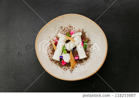 Gourmet dessert with white chocolate, biscuit shards, mint, and edible flowers on a textured plate Gourmet dessert with white chocolate, biscuit shards, mint, and edible flowers on a textured plate 118253007