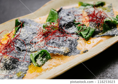 Gourmet squid ink ravioli with vibrant garnishes in a creamy sauce - an elegant and artistic dish 118253023