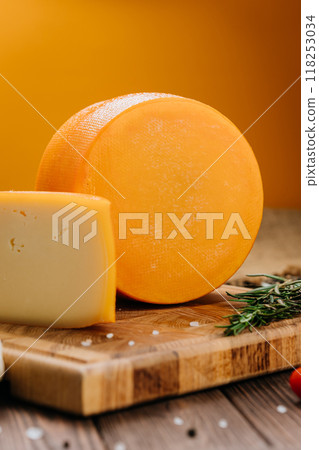 Golden cheese wheel and slice on wooden board, ideal for food photography and culinary presentations Golden cheese wheel and slice on wooden board, ideal for food photography and culinary presentations 118253034