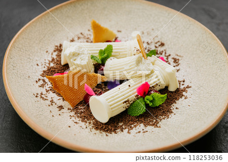 Gourmet dessert with white chocolate, biscuit shards, mint, and edible flowers on a textured plate 118253036