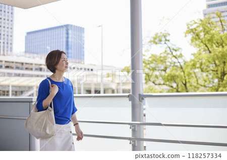 A full-body shot of a female office worker commuting on an elevated walkway at a train station. A full-body shot of a female office worker commuting on an elevated walkway at a train station. 118257334