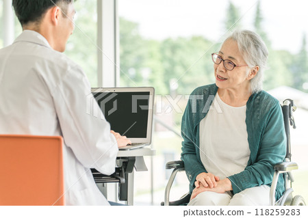 A senior woman explaining her condition to a doctor at a hospital or nursing facility and a male doctor asking her questions (medical examination, medical checkup, health check) 118259283
