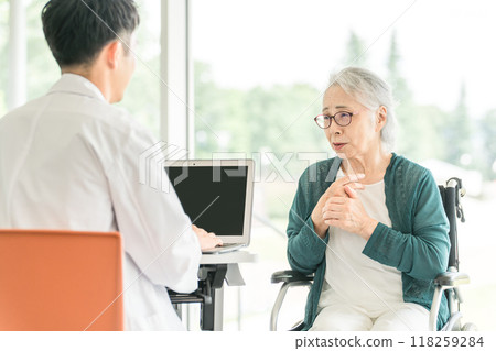 A senior woman explaining her condition to a doctor at a hospital or nursing facility and a male doctor asking her questions (medical examination, medical checkup, health check) 118259284