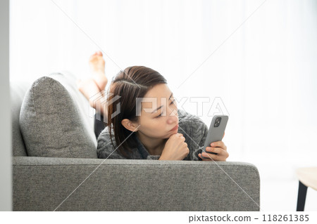 A woman lying down and looking at a smartphone 118261385