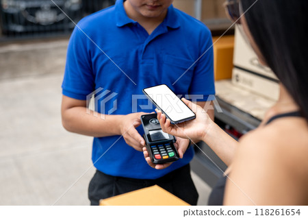 A customer tapping her smartphone on a card reader before receiving a package from a delivery man. A customer tapping her smartphone on a card reader before receiving a package from a delivery man. 118261654