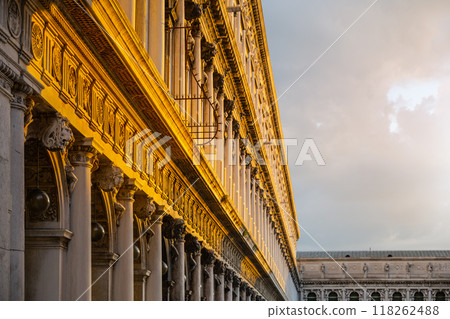 The intricate architectural features of the New Procuracie in Venice are highlighted by the warm glow of the setting sun, showcasing columns and ornate designs against a dramatic sky. The intricate architectural features of the New Procuracie in Venice are highlighted by the warm glow of the setting sun, showcasing columns and ornate designs against a dramatic sky. 118262488