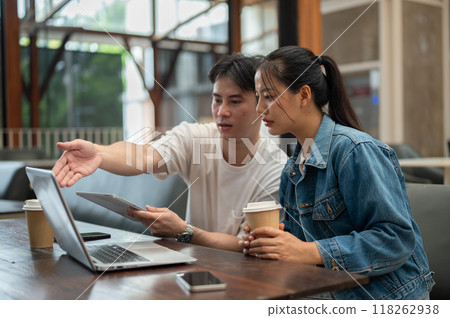 Two Asian college friends or colleagues are discussing work at a coffee shop, sharing their ideas. 118262938