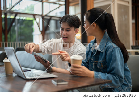 Two Asian college friends or colleagues are discussing work at a coffee shop, sharing their ideas. 118262939