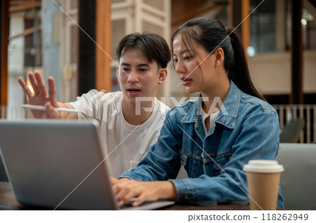 Two positive Asian friends or colleagues are working remotely together from a coffee shop. 118262949