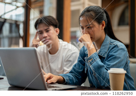 A stressed Asian woman working on her laptop while discussing a work issue with her male colleague. A stressed Asian woman working on her laptop while discussing a work issue with her male colleague. 118262950