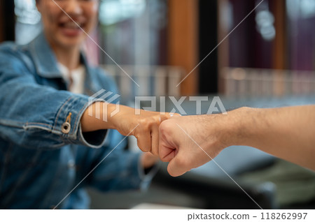 A close-up of two people giving each other a fist bump during a meeting at a coffee shop. 118262997
