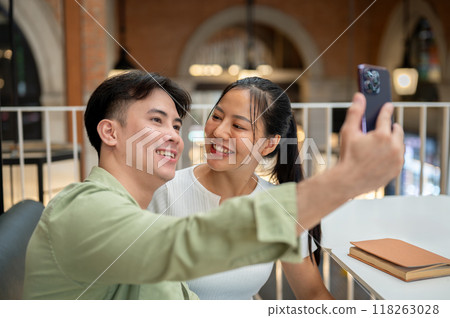 A lovely Asian couple are enjoying taking selfies together with a phone while on a date at a cafe. 118263028