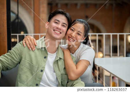 A lovely, happy young Asian couple is taking a selfie together while on a date at a coffee shop. A lovely, happy young Asian couple is taking a selfie together while on a date at a coffee shop. 118263037