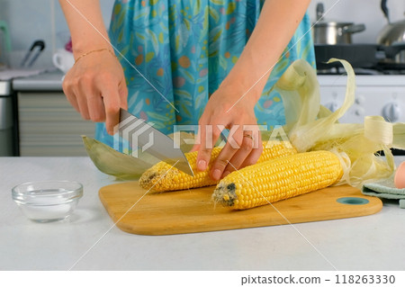 Woman cutting fresh corn on wooden board cooking vegetable dish at home. 118263330
