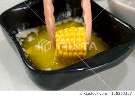 Woman dipping piece of fresh sweet corn in melted butter cooking on kitchen. 118263337