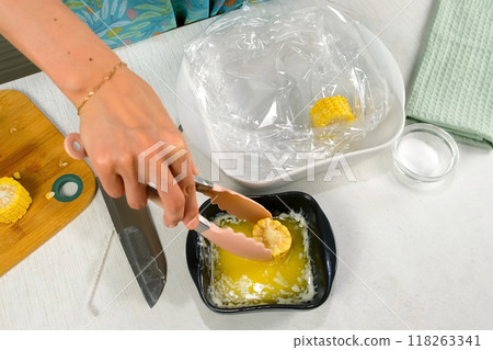 Woman dipping piece of fresh corn in melted butter putting it in baking sleeve. 118263341