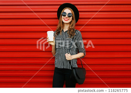 Stylish young woman with coffee cup in black shirt, round hat, handbag clutch on red wall background Stylish young woman with coffee cup in black shirt, round hat, handbag clutch on red wall background 118265775